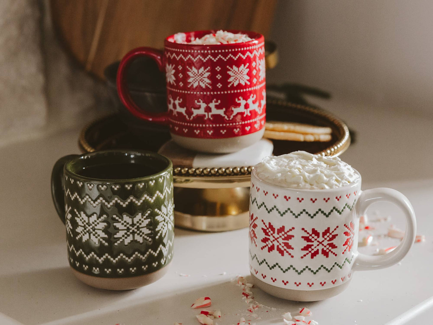 Red Fair Isle stoneware coffee mug filled with hot cocoa and styled with evergreen branches, pinecones, and cozy knit textiles.