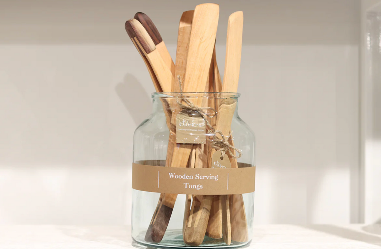 Set of wooden serving utensils in a glass jar with a label on a neutral background
