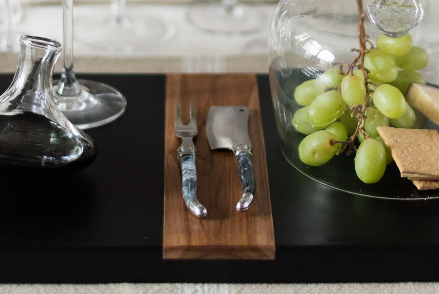 Wooden cutting board with knife and fork on a black surface with grapes in a jar.