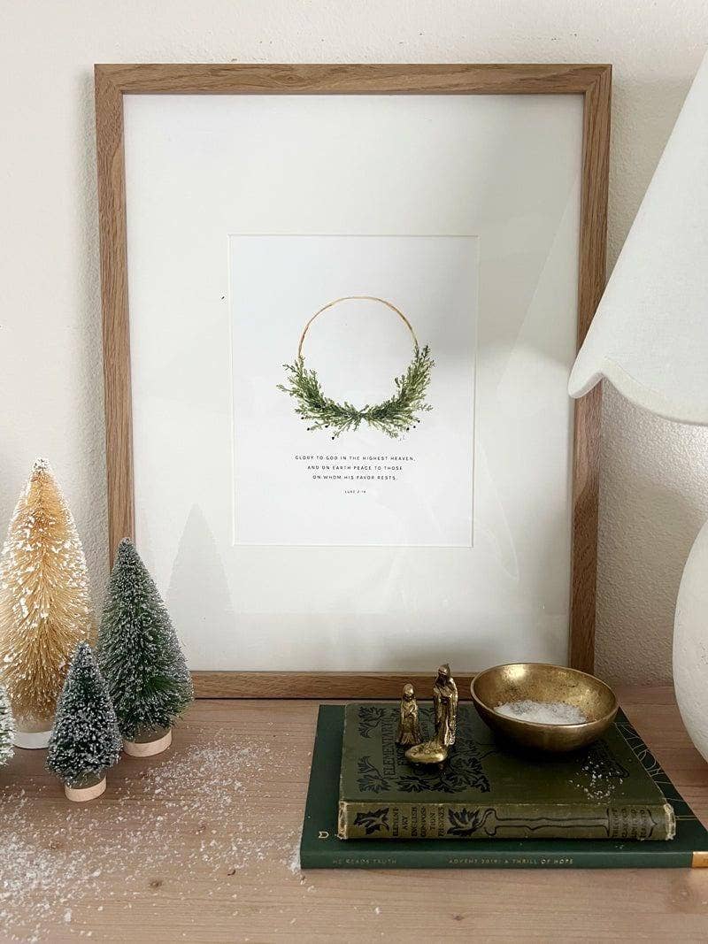 Framed Luke 2:14 Wreath Scripture print displayed on a Christmas mantel with evergreen garland, candles, and natural holiday décor.