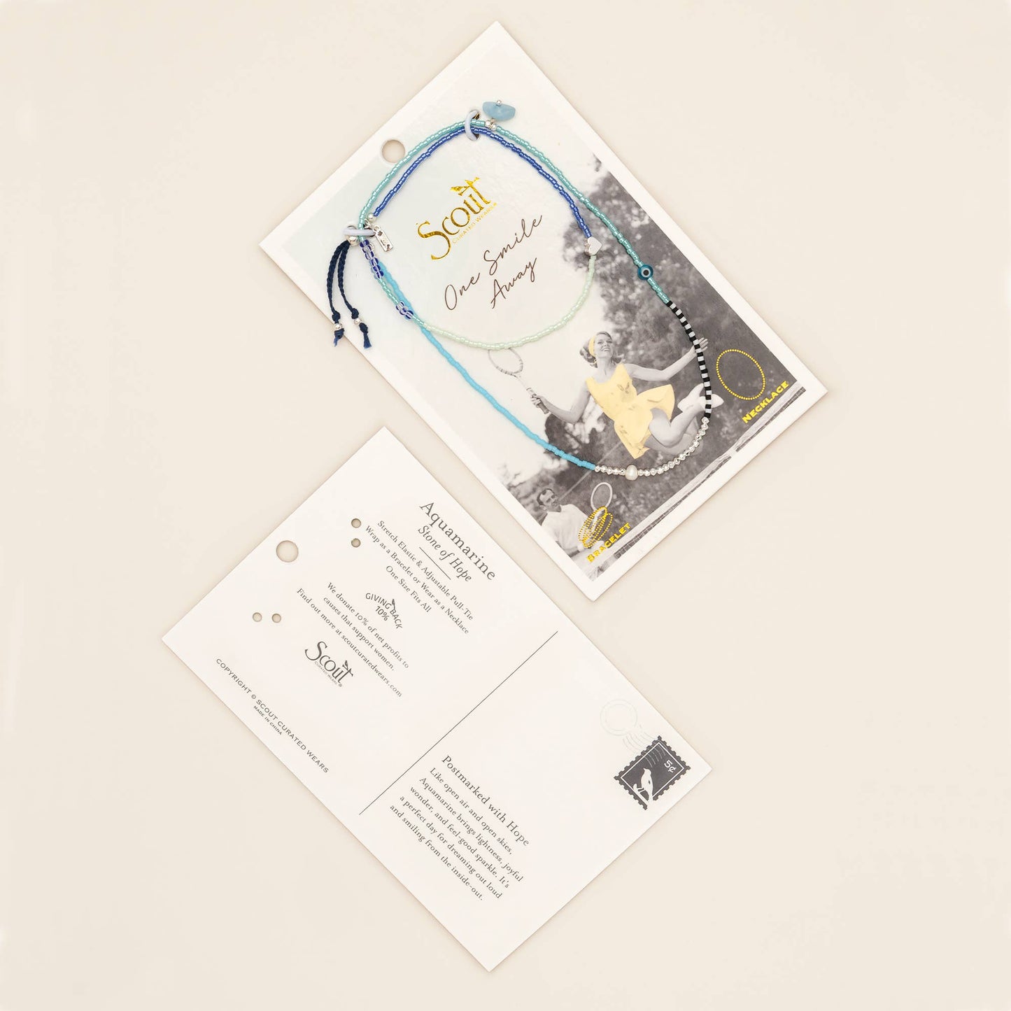 Convertible aquamarine wrap jewelry displayed on its keepsake postcard beside natural linen, fresh flowers, and thoughtful gift wrapping.