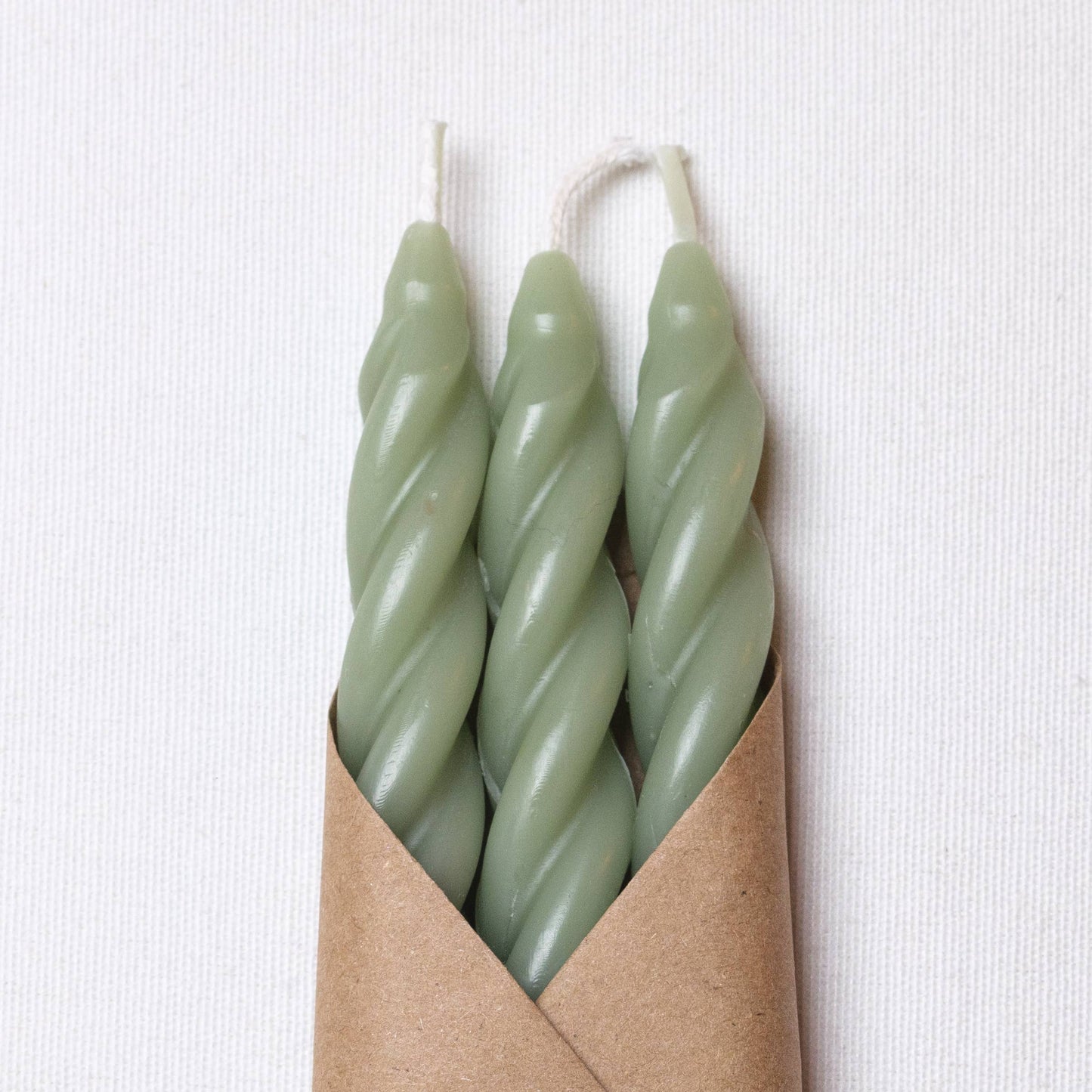 Set of three handcrafted spiral beeswax taper candles in a soft sage green color.