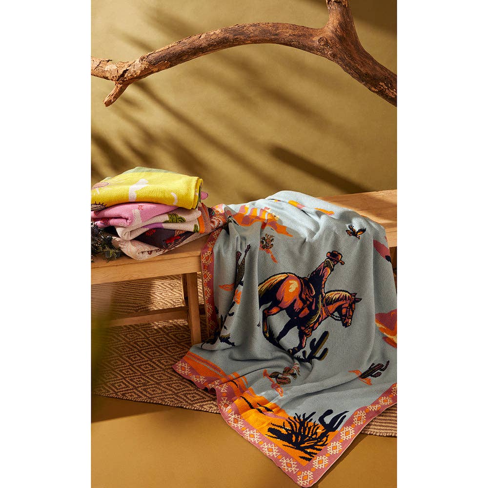 Lone Bronco Rider Woven Throw Blanket featuring a cowboy riding a bucking bronco beneath a dusty blue prairie sky with a tribal-inspired border.