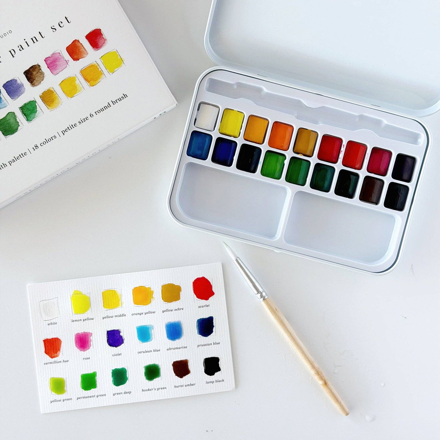 Portable watercolor paint set paired with an Emily Lex watercolor workbook on a wooden table, creating a peaceful space for creativity.