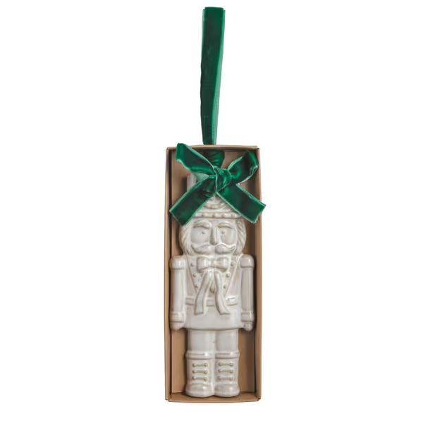 White stoneware nutcracker ornament with a reactive glaze finish and velvet ribbon.