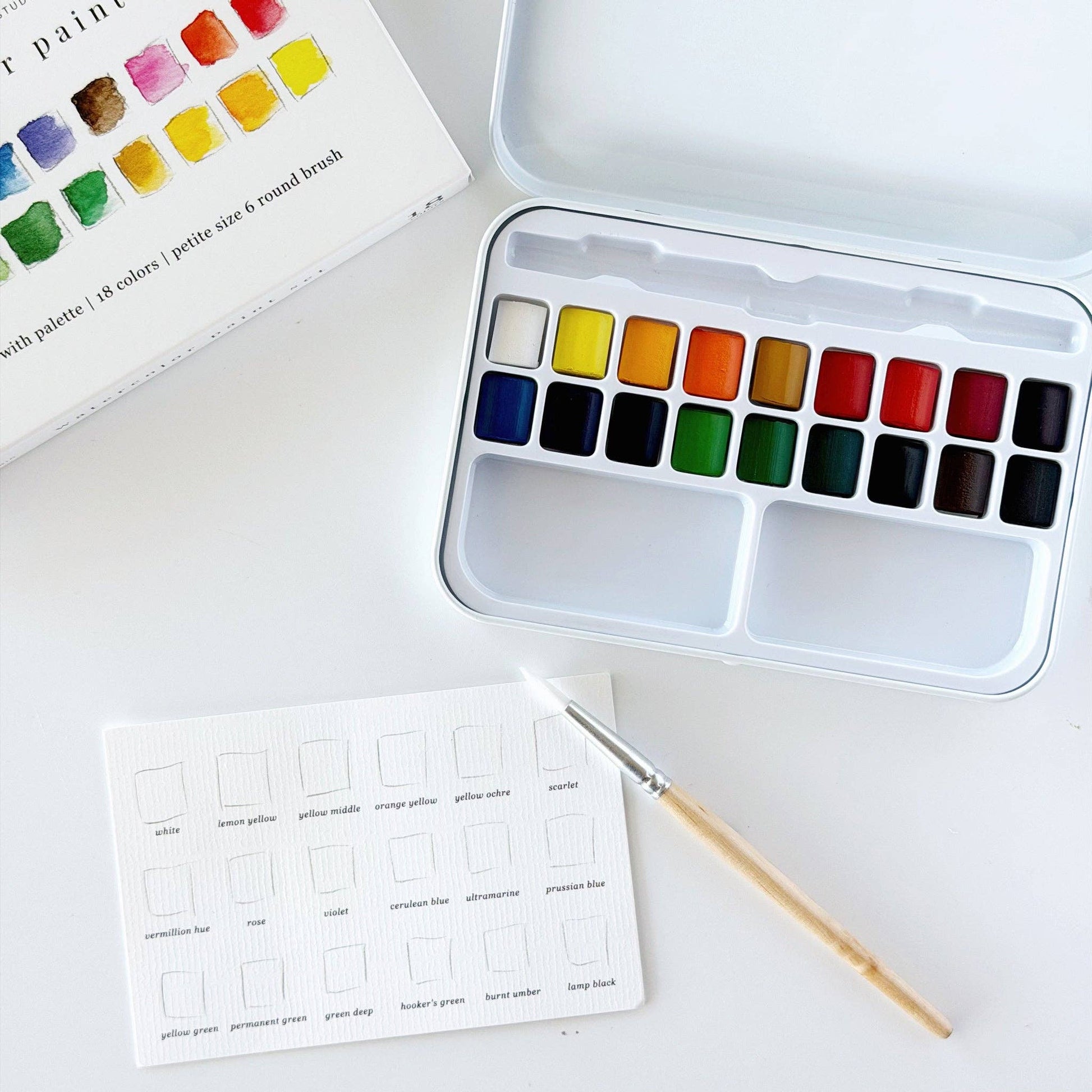 Portable watercolor paint set paired with an Emily Lex watercolor workbook on a wooden table, creating a peaceful space for creativity.