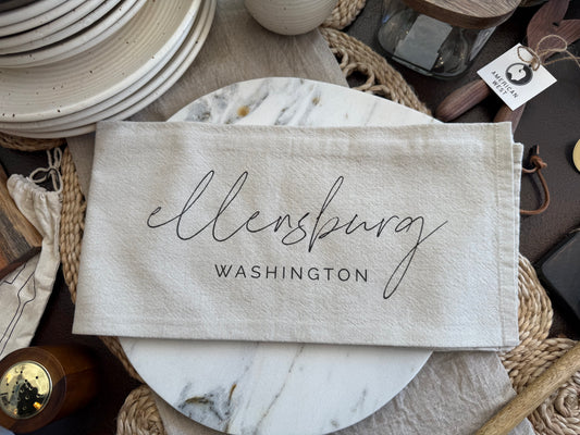 Fabric tea towel with 'Ellensburg, Washington' text on a rustic background