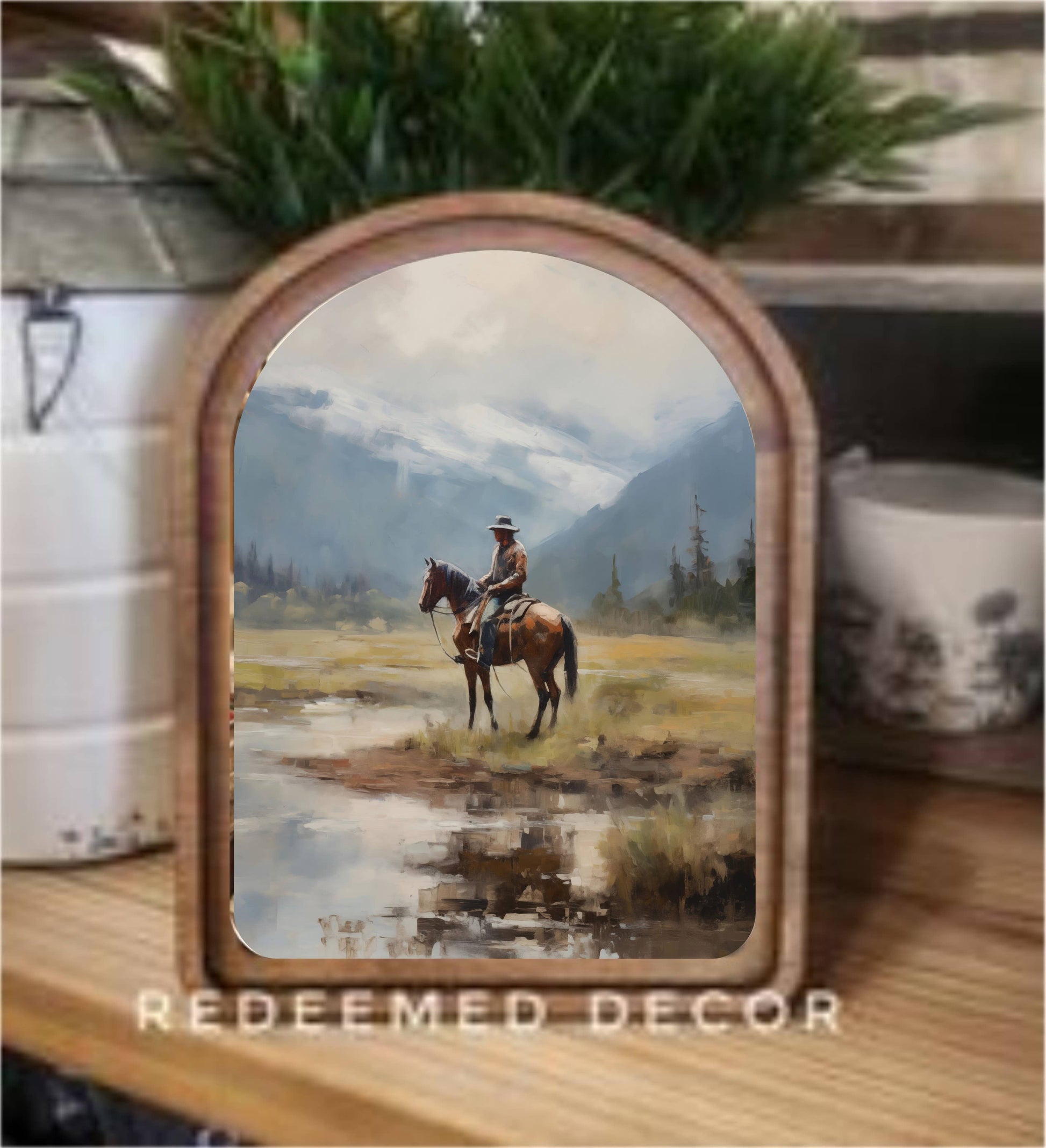 Arch Top Mountain Cowboy Framed Canvas Art featuring a cowboy riding through a mountain landscape in a handcrafted arched wood frame with an Early American finish.