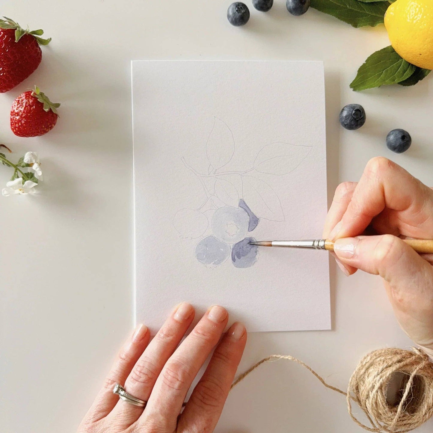 Watercolor fruit notecard set styled on a desk with art supplies, fresh citrus, and botanical accents, creating an inviting creative gift display.