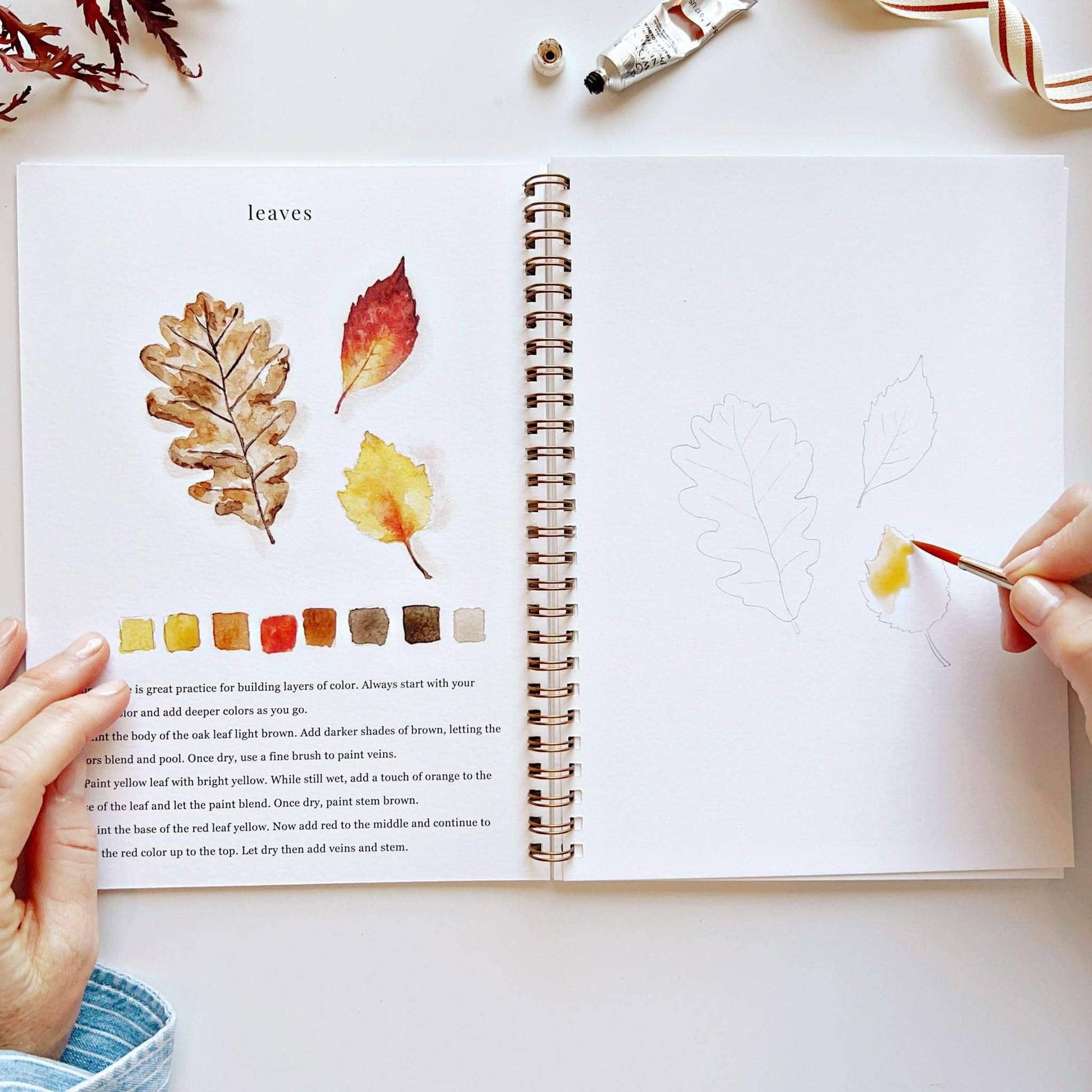 Autumn Watercolor Workbook displayed with watercolor paints and brushes.