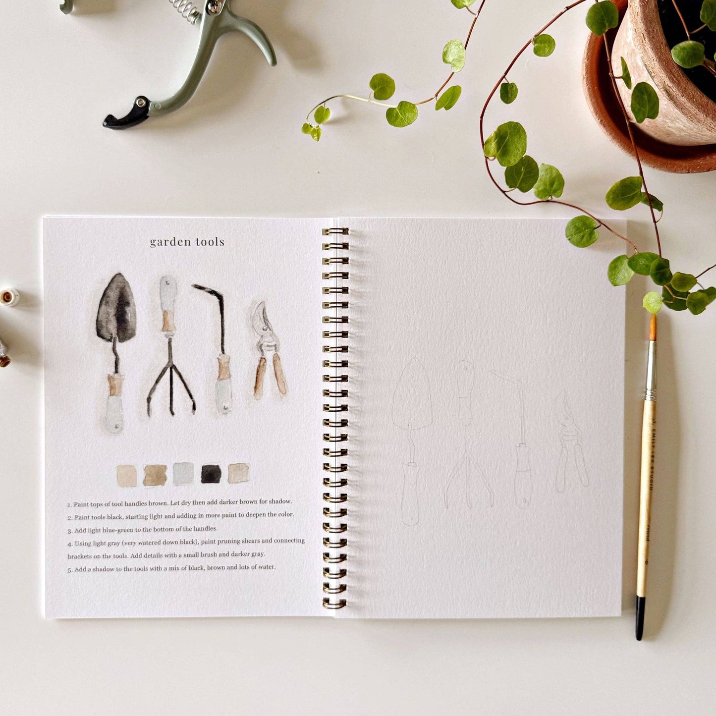 Botanical watercolor workbook styled with paints and brushes on an art table.