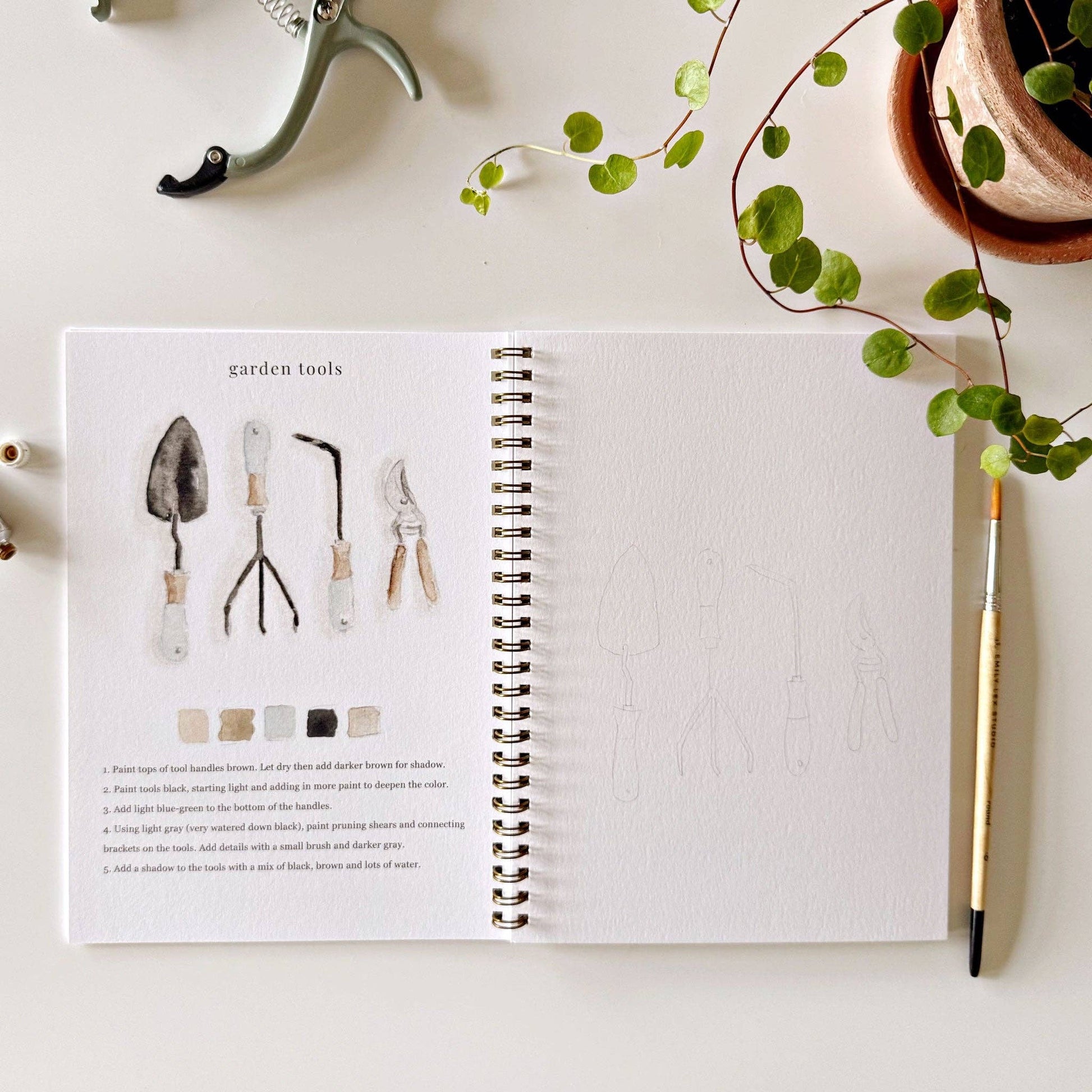 Botanical watercolor workbook styled with paints and brushes on an art table.