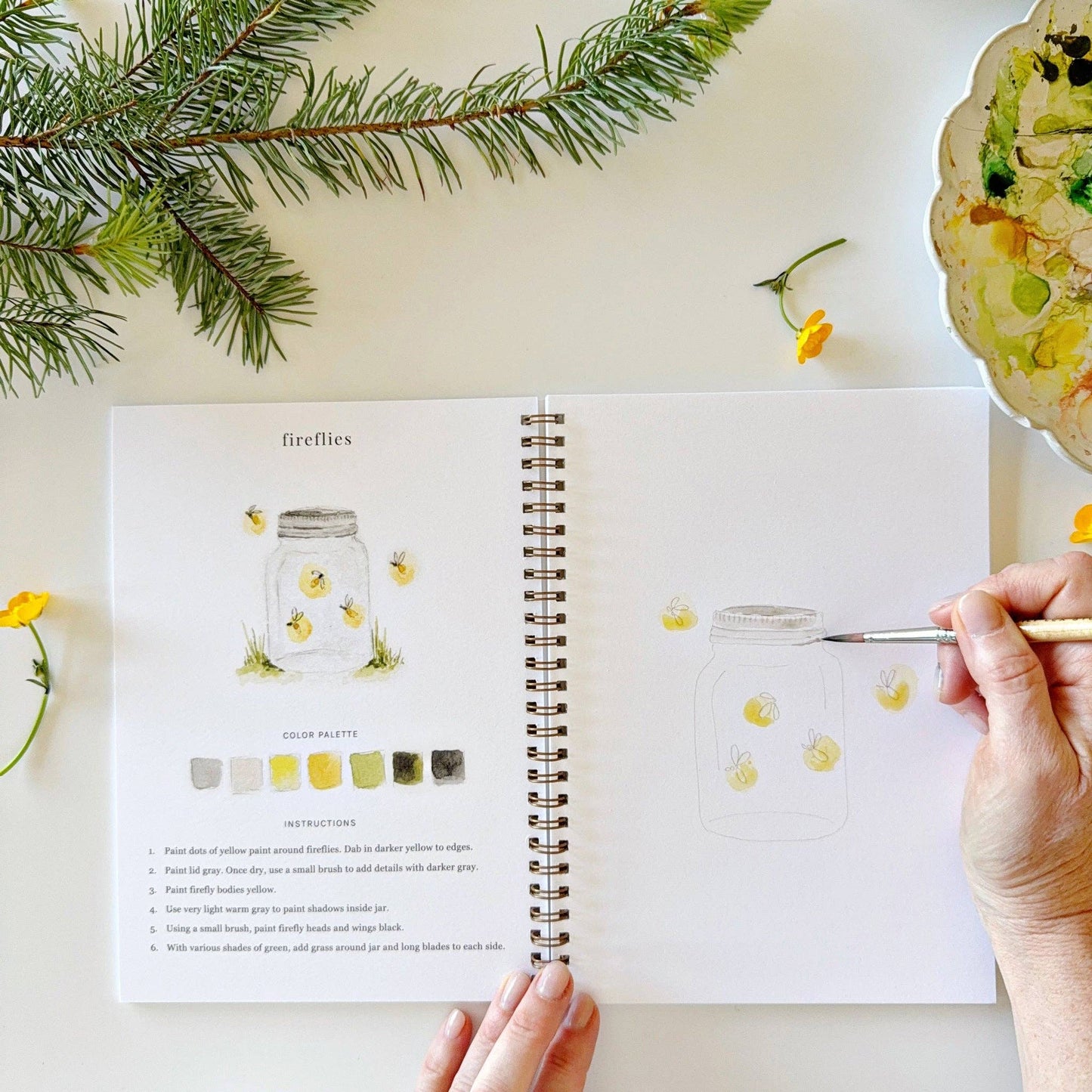 Spiral-bound watercolor workbook with lightly sketched camping-themed artwork.