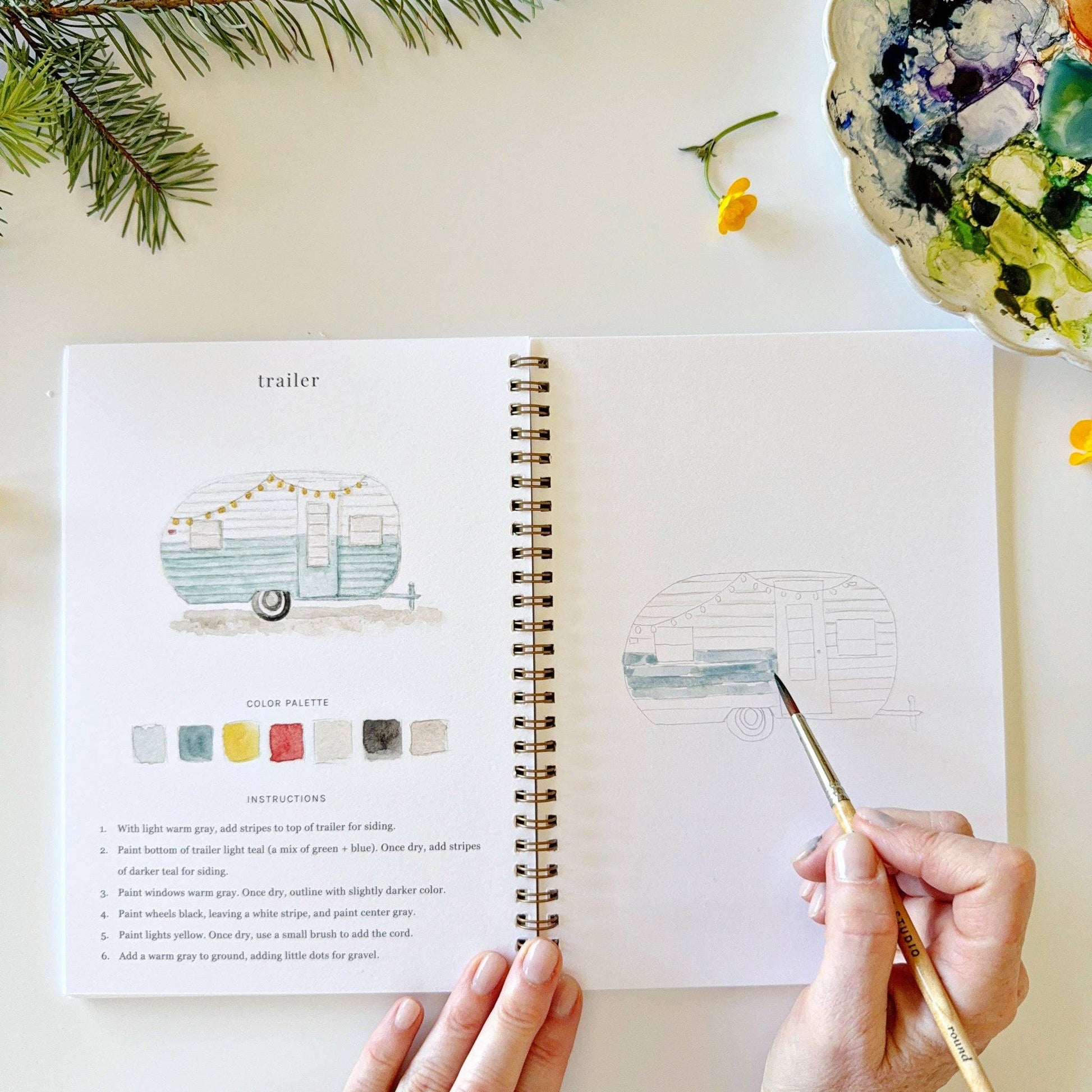 Camping watercolor workbook paired with paints and brushes for a relaxing creative activity.