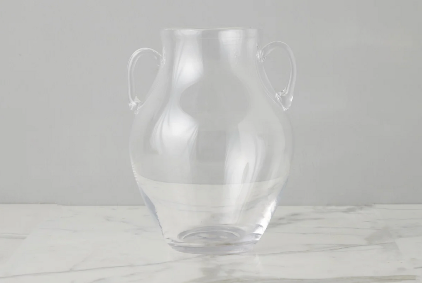 Clear glass vase with handles on a light gray background