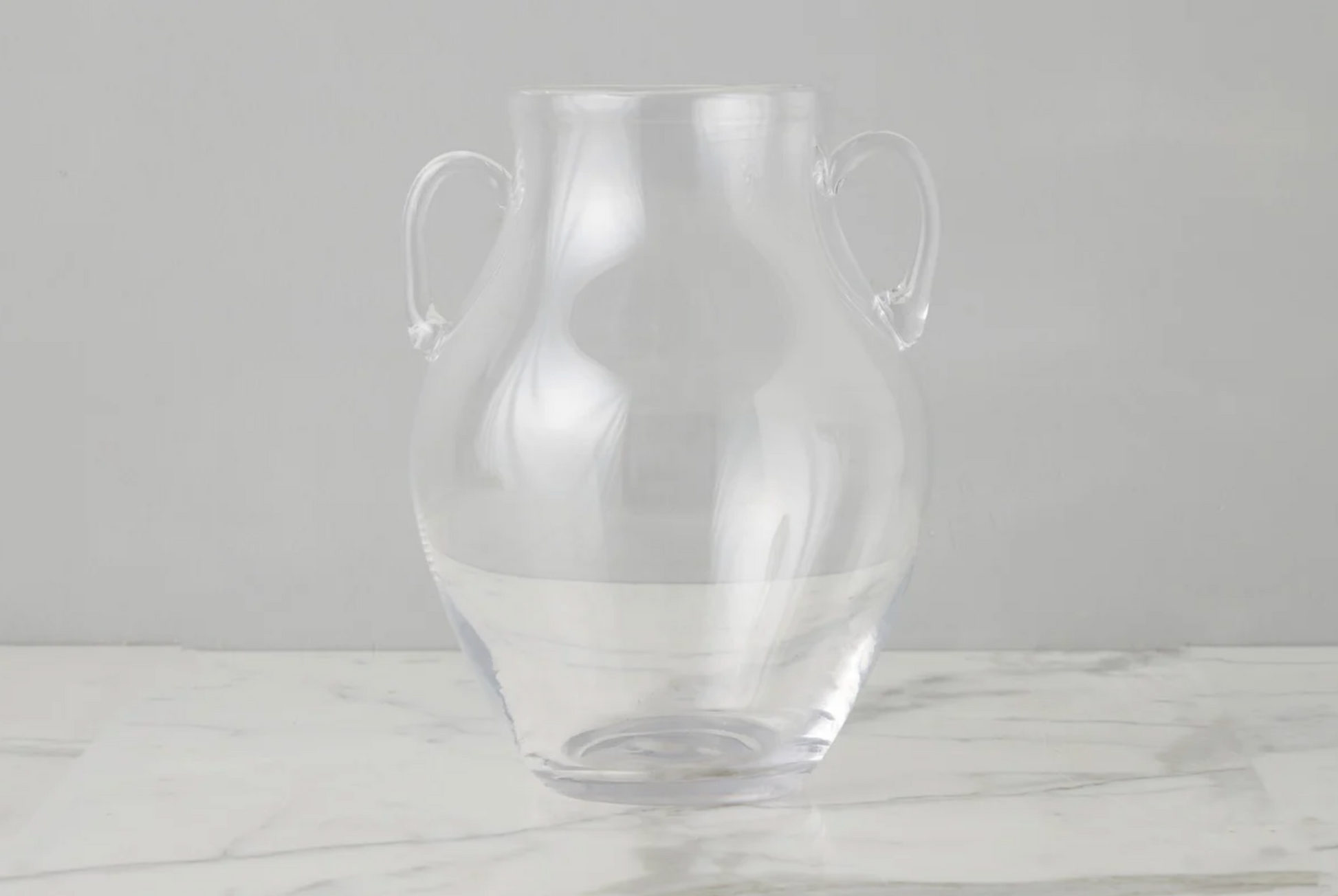 Clear glass vase with handles on a light gray background