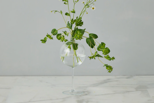 Clear glass vase with greenery on a marble surface and light gray background
