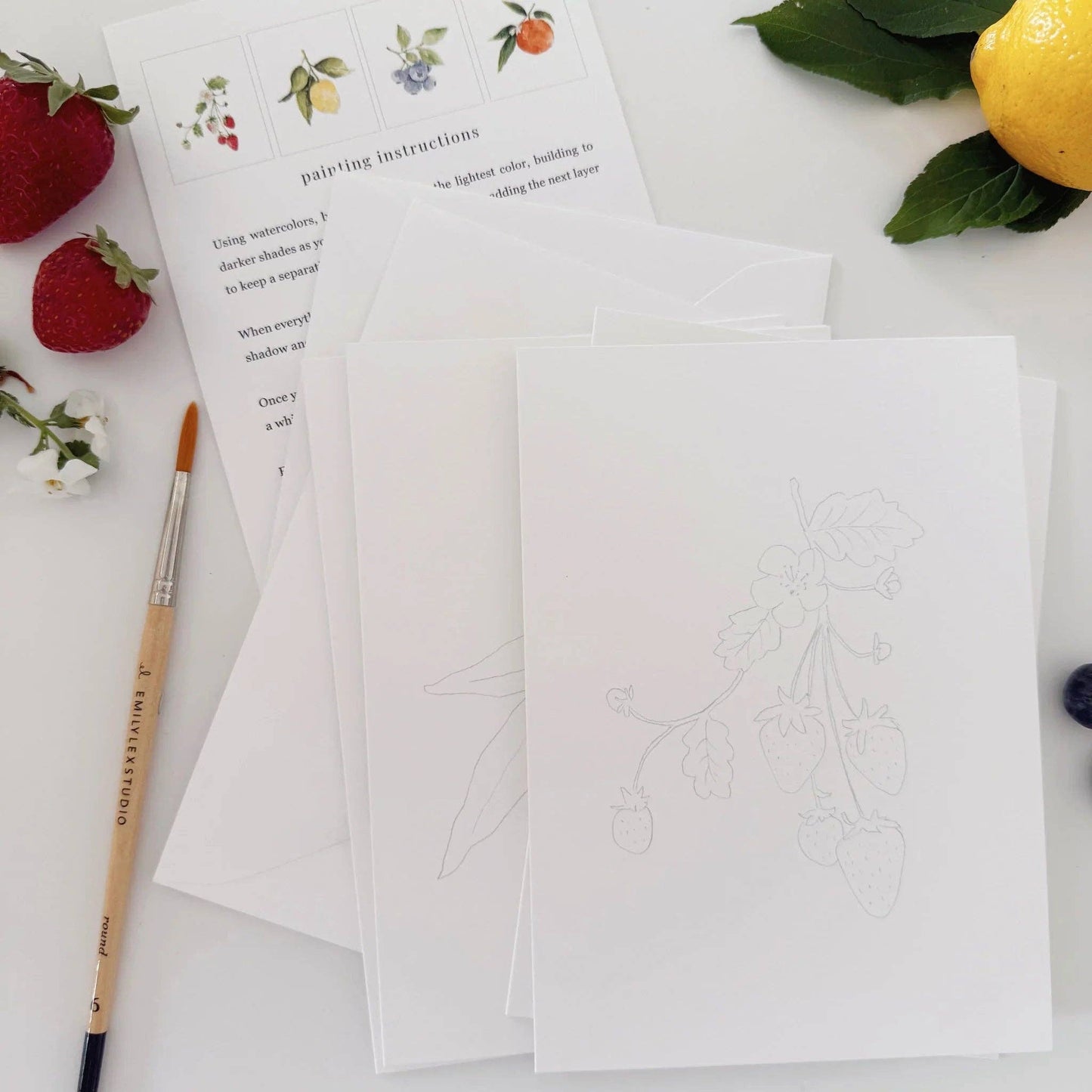 Paintable watercolor notecard set displayed with watercolor paints, brushes, and envelopes on a bright creative workspace.