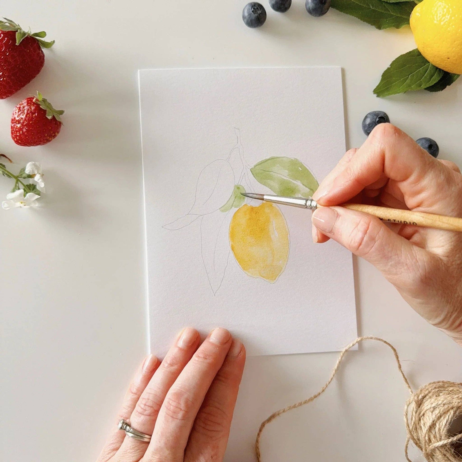 Paintable watercolor notecard set displayed with watercolor paints, brushes, and envelopes on a bright creative workspace.