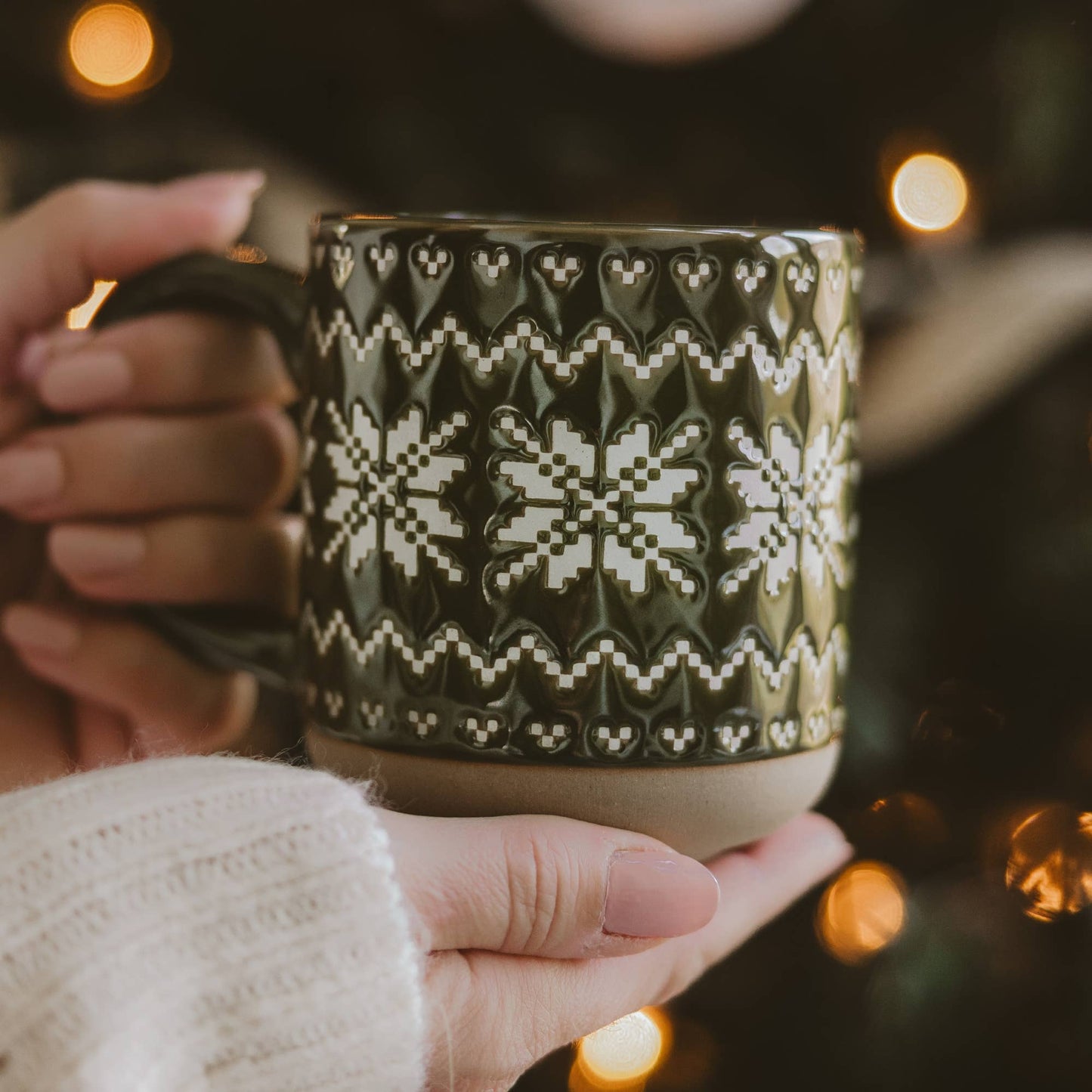 Green Fair Isle stoneware mug filled with coffee and styled with evergreen branches, knit blankets, and holiday décor.