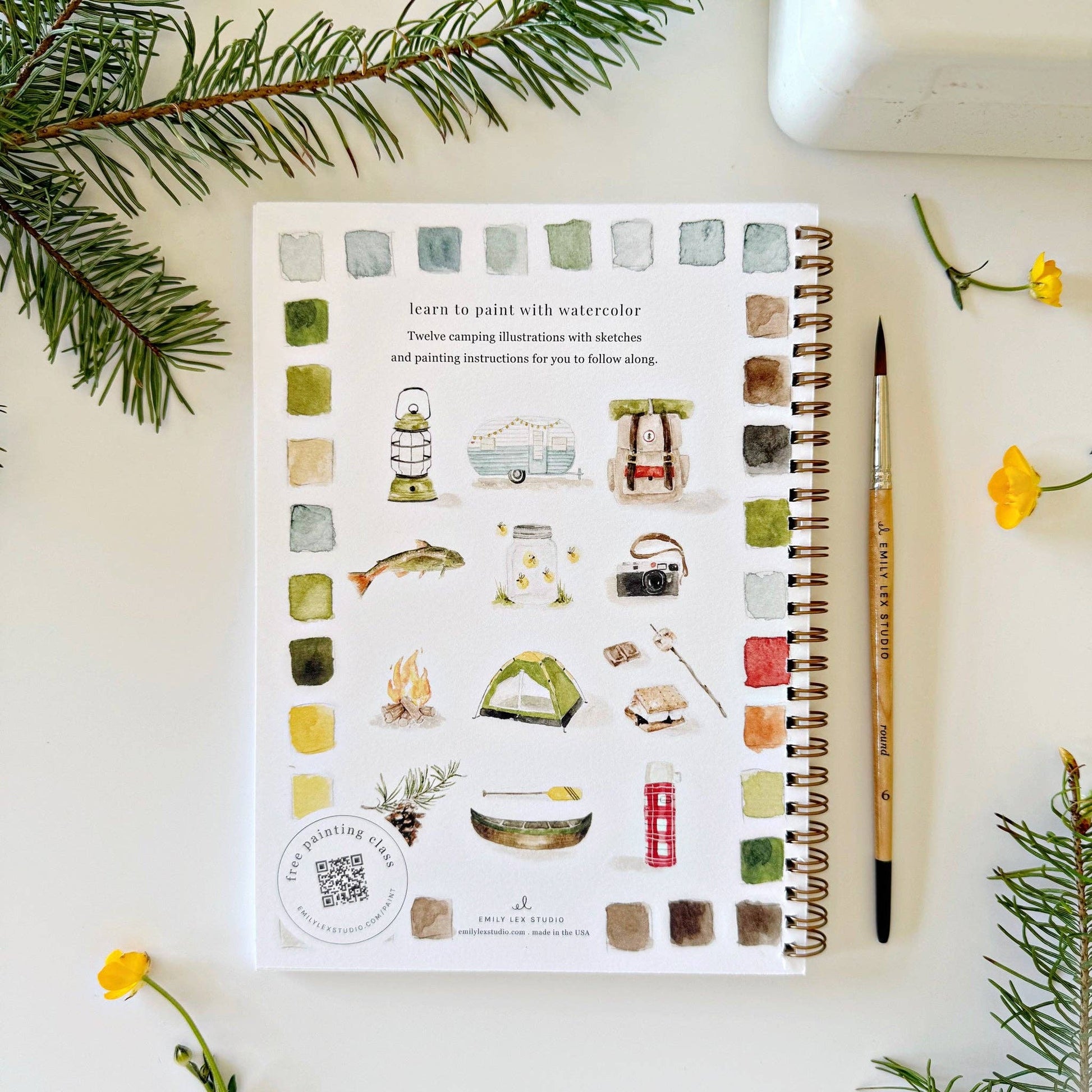 Spiral-bound watercolor workbook with lightly sketched camping-themed artwork.