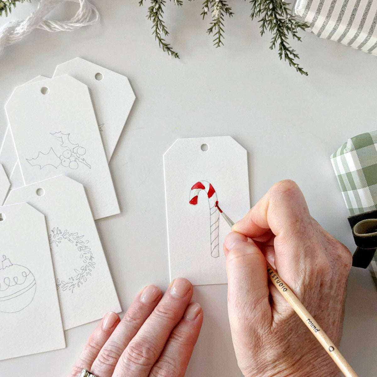 Hand-painted Emily Lex Christmas gift tags tied onto wrapped holiday presents with the included string.
