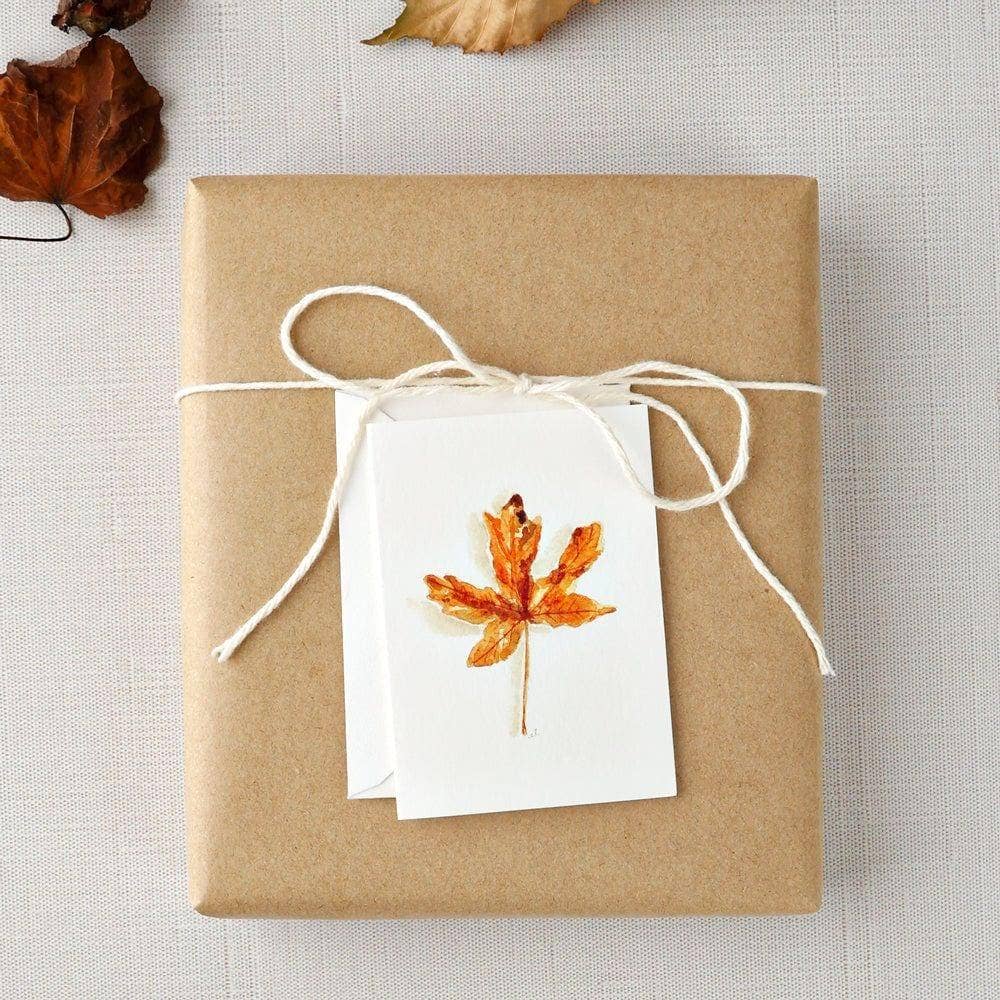 Autumn maple leaf mini enclosure card tucked into a wrapped gift with twine, dried foliage, and kraft paper.