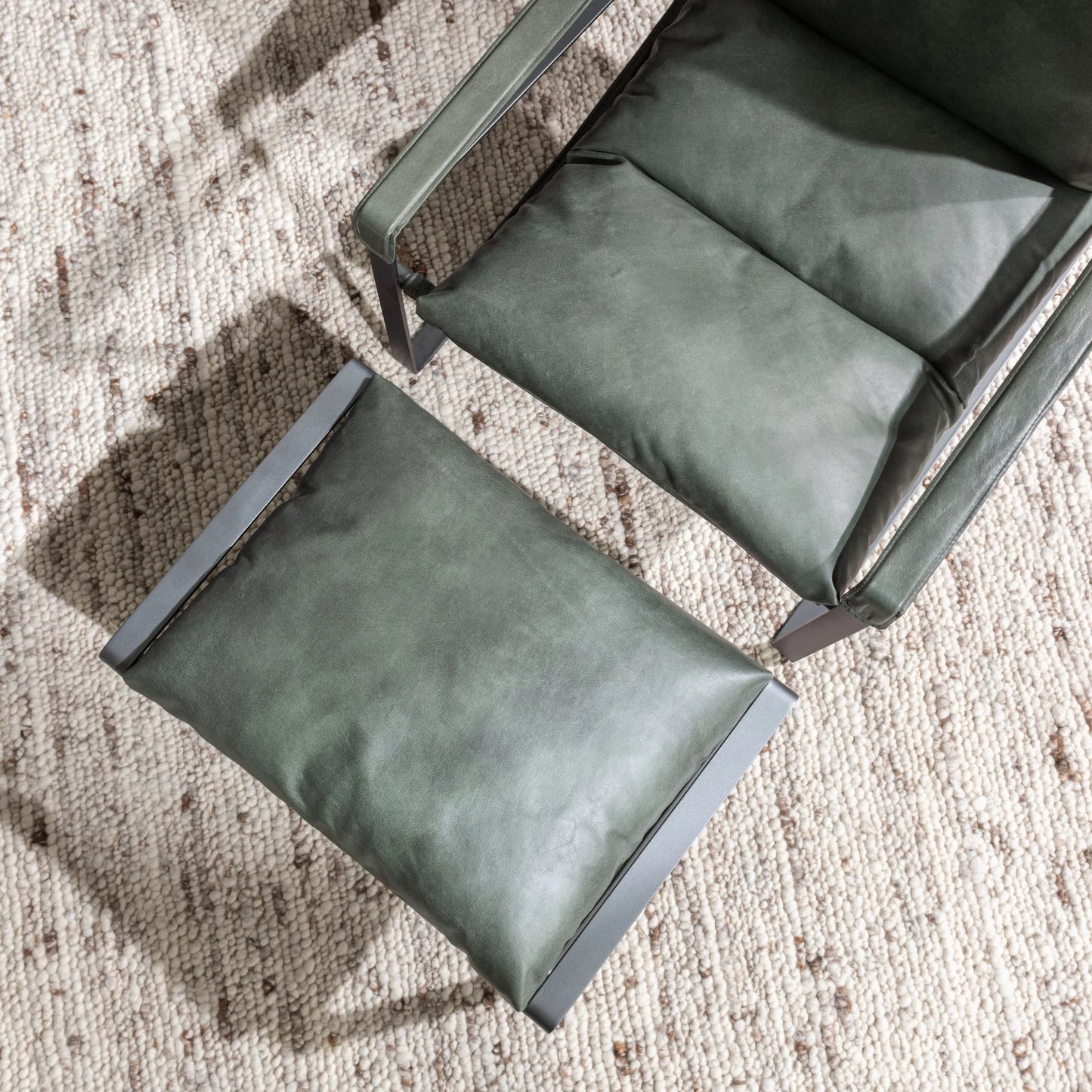 Forest green leather ottoman styled in an organic modern living room with leather accent chair and neutral textured area rug.
