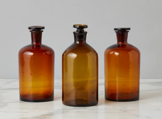 Three amber glass bottles with black lids on a light gray background