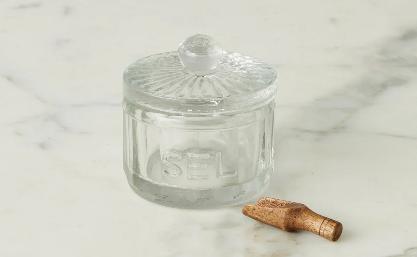 Clear glass jar with a lid and wooden spoon on a marble surface