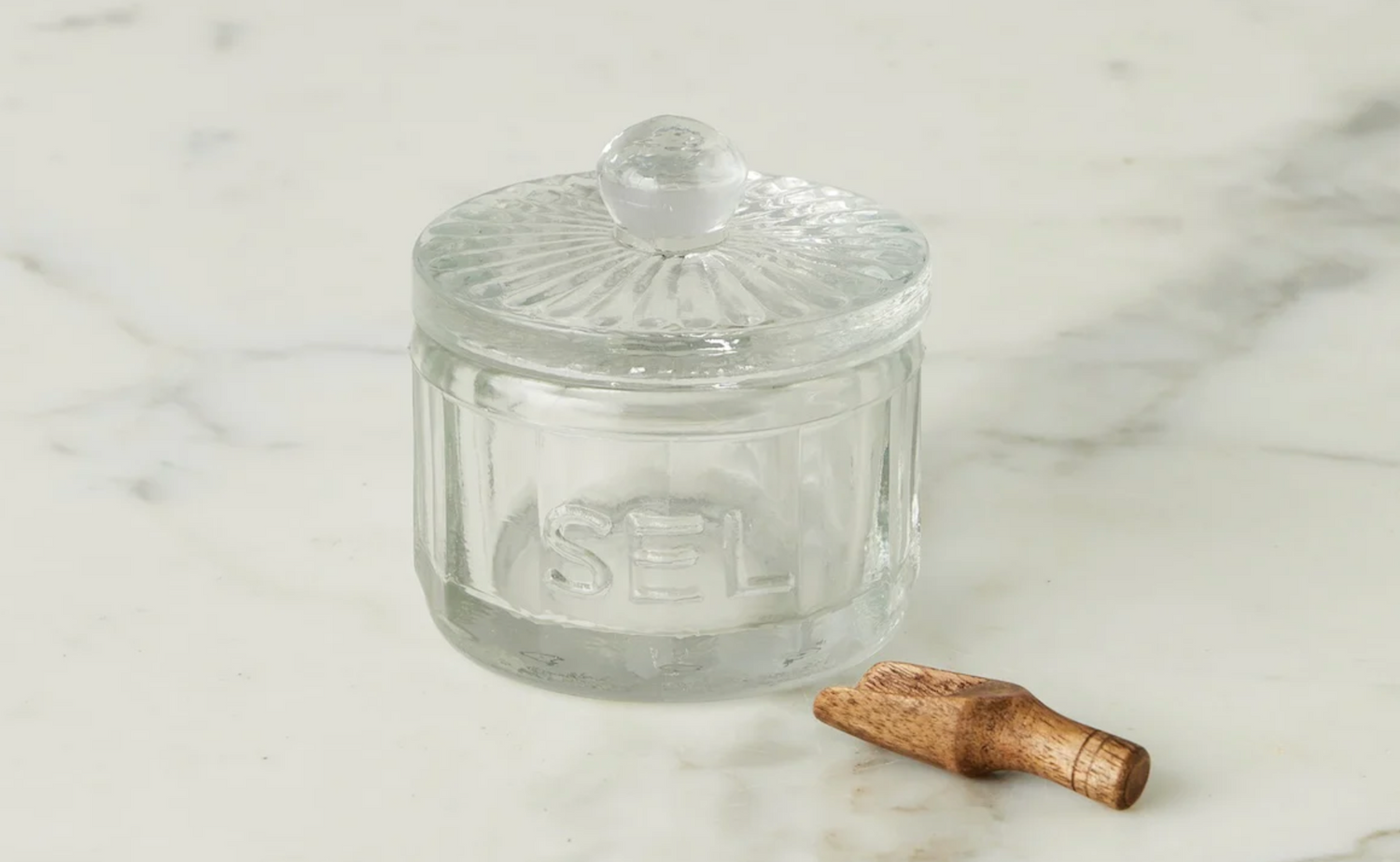 Clear glass jar with a lid and wooden spoon on a marble surface