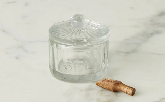 Clear glass jar with a lid and wooden spoon on a marble surface