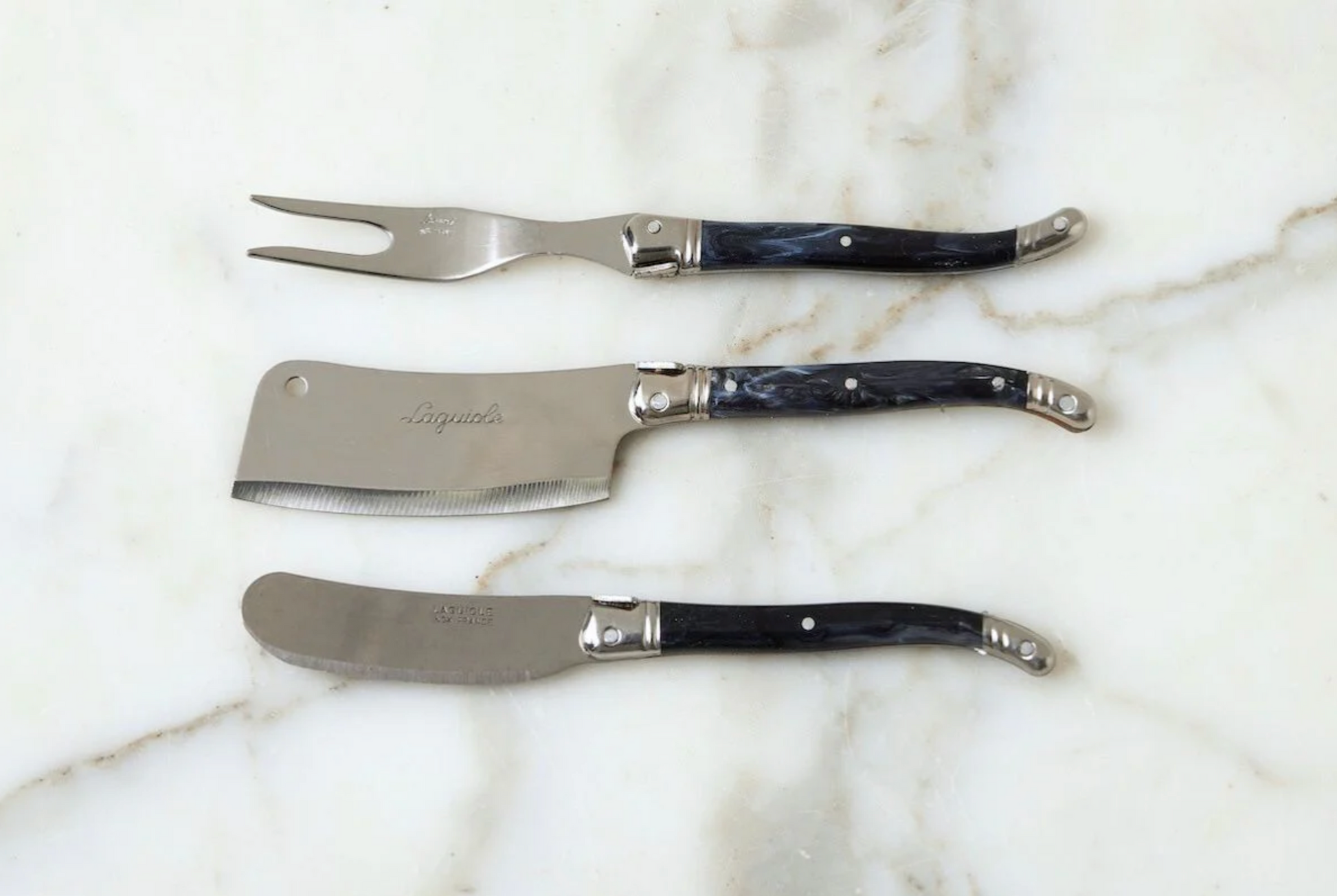 Three metal utensils with black handles on a marble surface