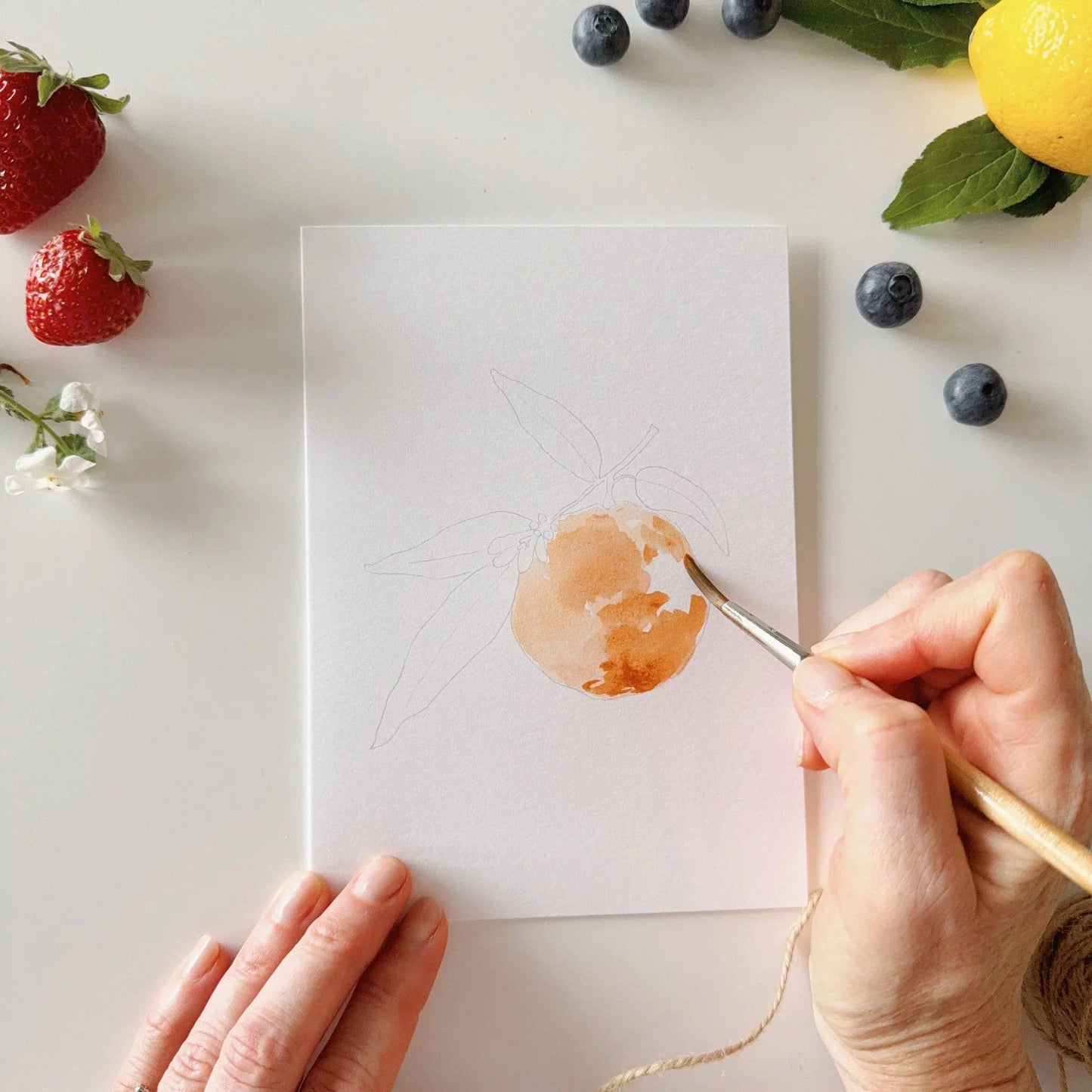 Watercolor fruit notecard set styled on a desk with art supplies, fresh citrus, and botanical accents, creating an inviting creative gift display.