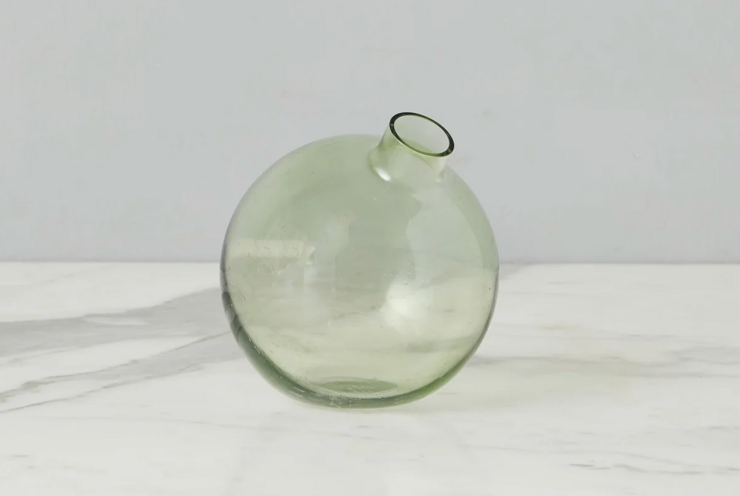 Green glass vase on a white surface with a light gray background