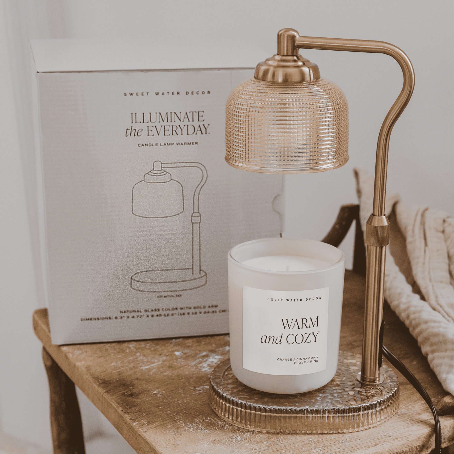 Glass candle lamp warmer with a neutral glass shade, gold adjustable arm, and elegant flameless design.