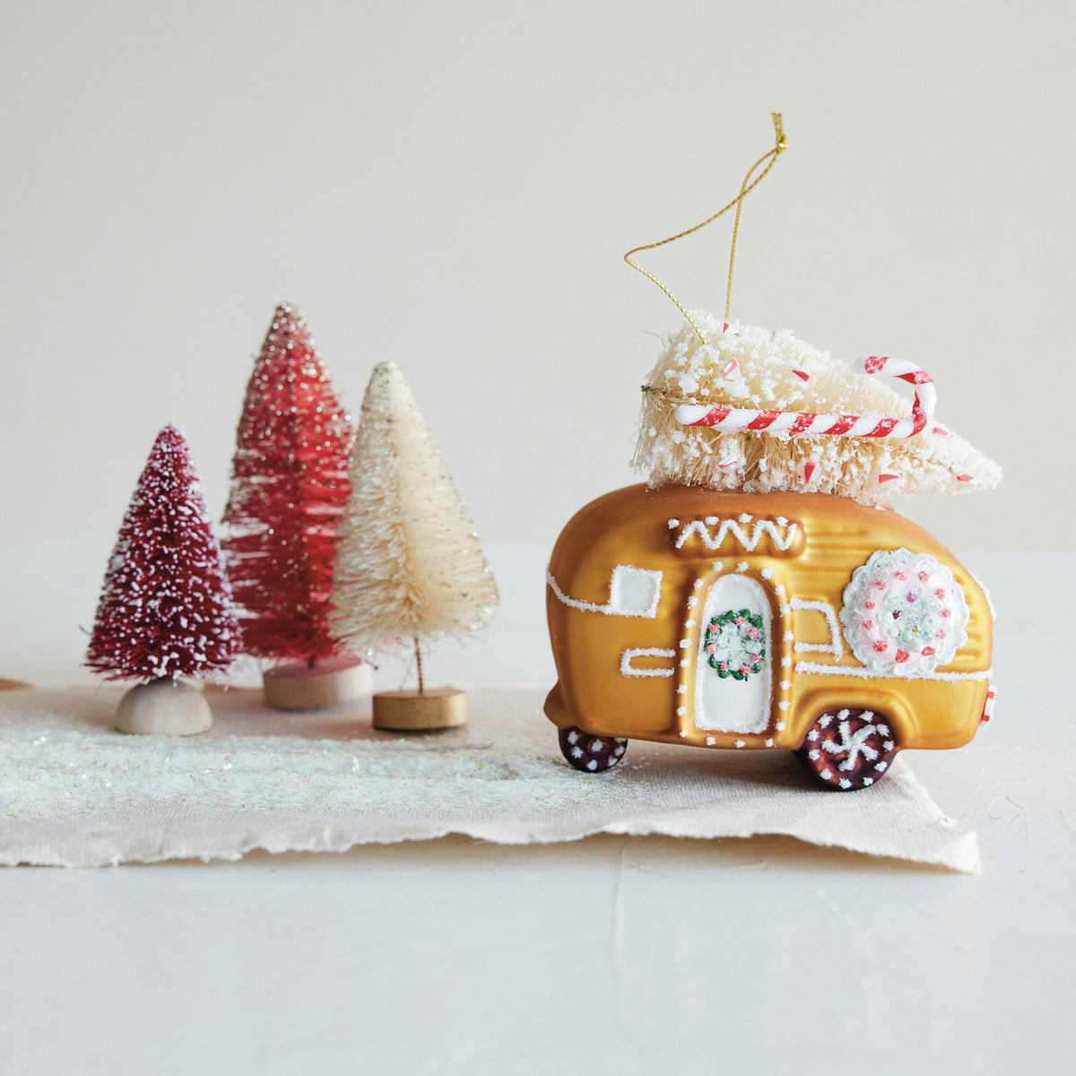 Hand-painted gingerbread camper glass Christmas ornament with a bottle brush tree, wreath, candy cane details, and glitter.