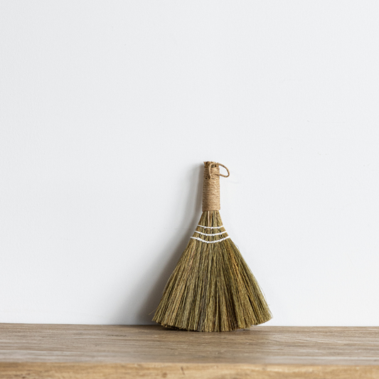 Handwoven seagrass handle broom styled as a decorative accent in an entryway or kitchen