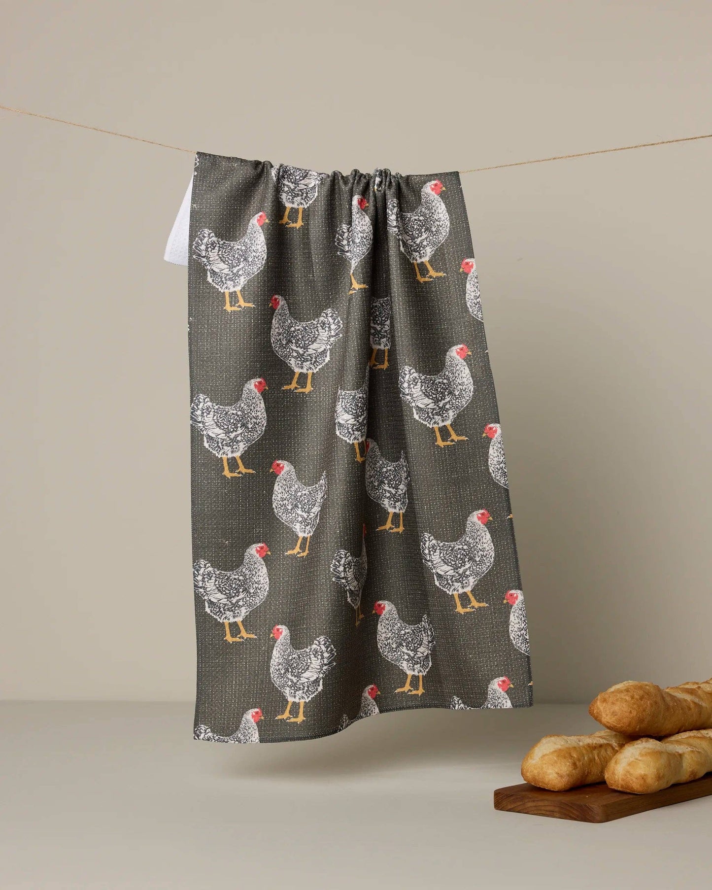 Towel with chicken pattern hanging on a line against a beige background