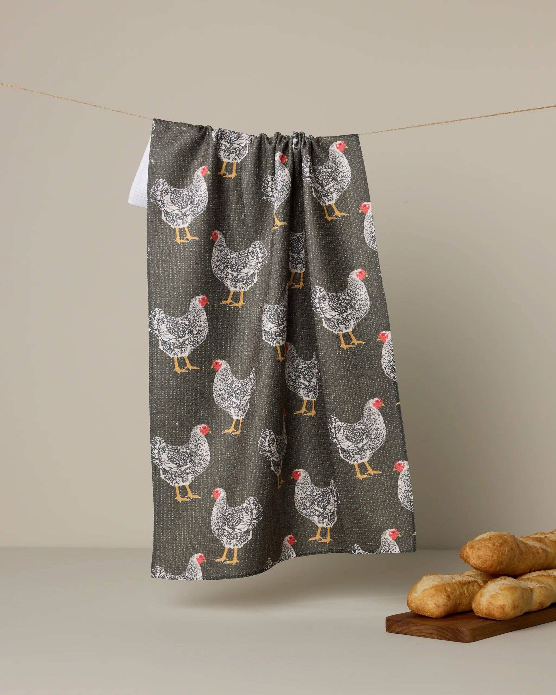 Towel with chicken pattern hanging on a line against a beige background