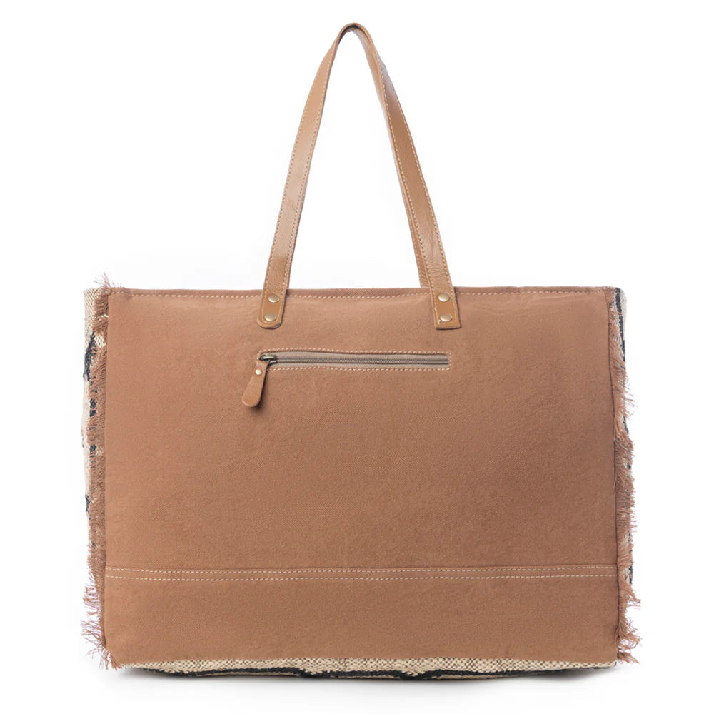 Kaliko Hill Weekender Bag featuring a woven tribal-inspired rug textile, caramel leather straps, and a spacious zip-top design.