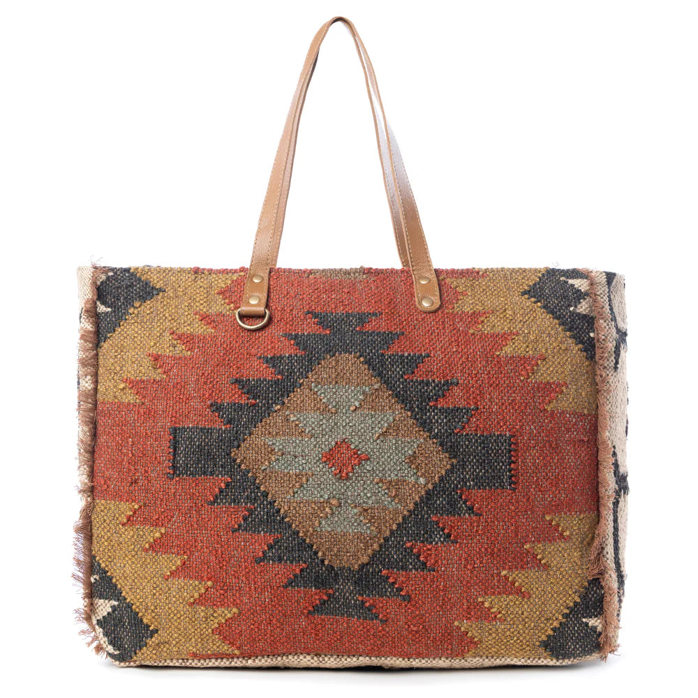 Kaliko Hill Weekender Bag featuring a woven tribal-inspired rug textile, caramel leather straps, and a spacious zip-top design.
