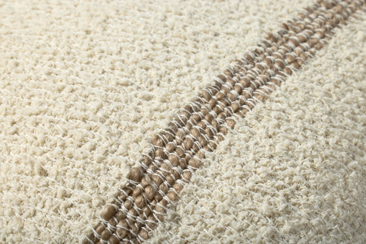 Close-up of the woven cotton and polyester pillow highlighting the natural texture, flange edge, and hidden zipper with antique bronze Loloi logo pull.