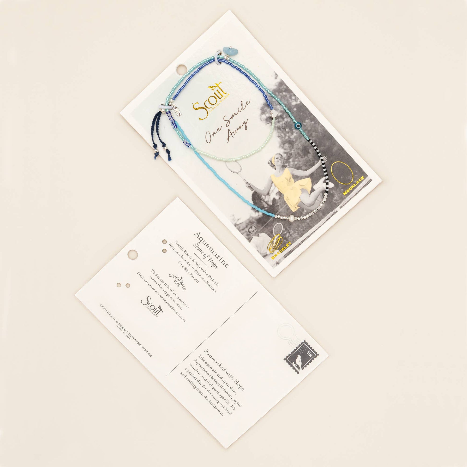 Convertible aquamarine wrap jewelry displayed on its keepsake postcard beside natural linen, fresh flowers, and thoughtful gift wrapping.