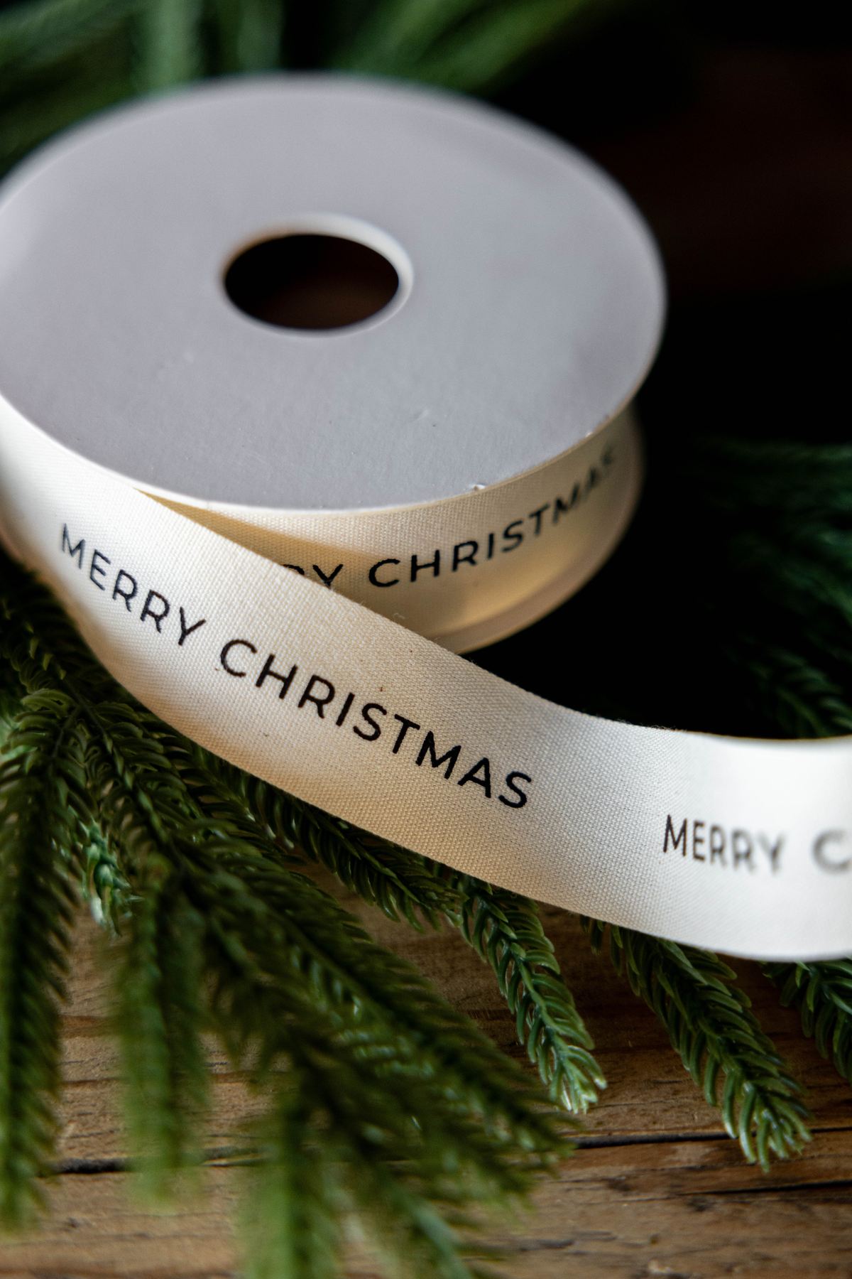Spool of natural holiday ribbon with black Merry Christmas lettering, measuring 5 yards long.