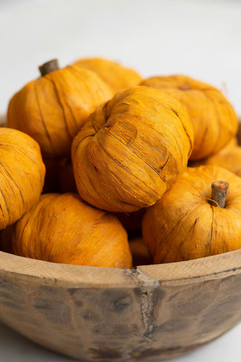 Mini faux pumpkins displayed in a wooden bowl as an autumn centerpiece.