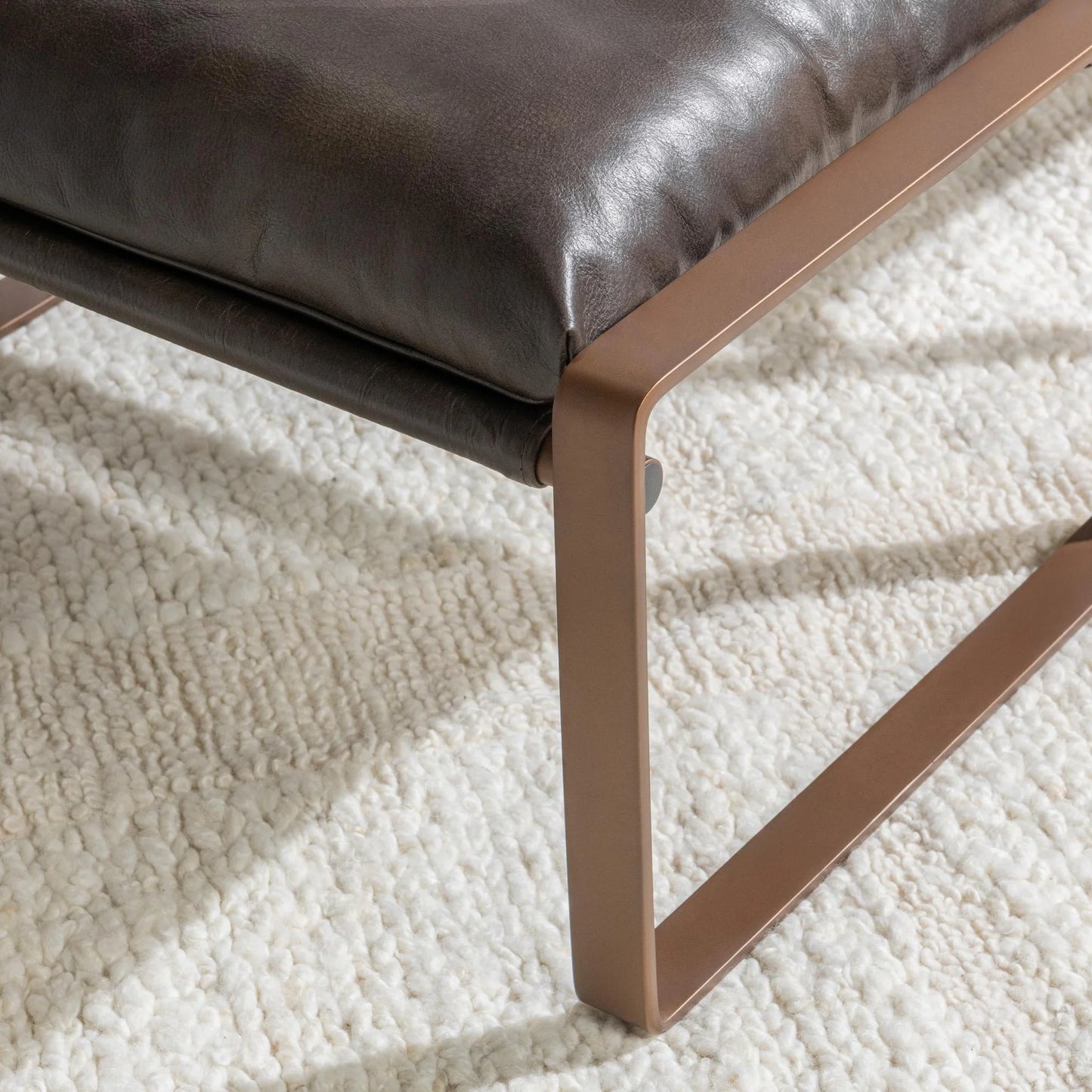 Close-up of the Morgan ottoman showcasing the rich texture of the top grain leather cushion and minimalist iron frame.