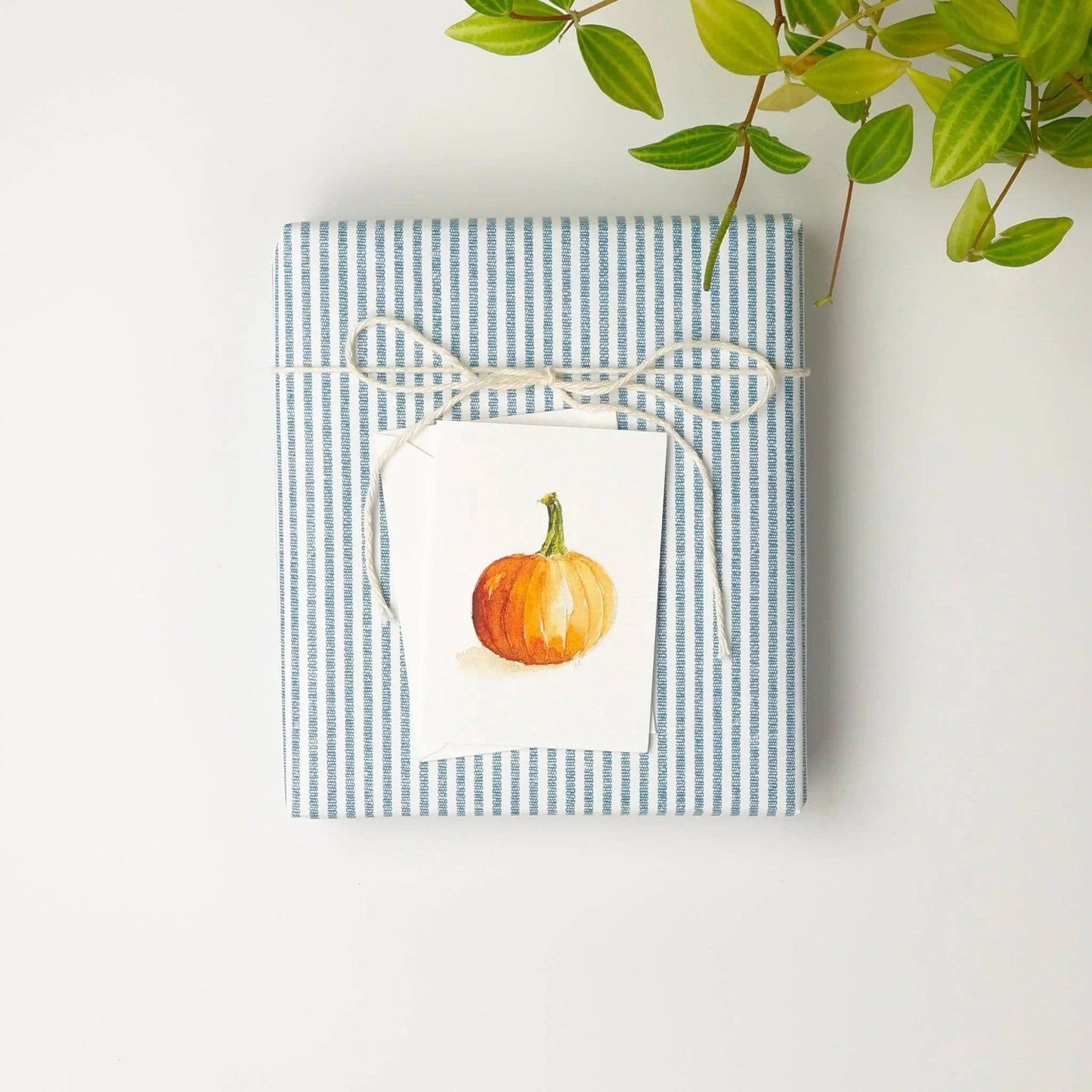 Orange pumpkin mini enclosure card tucked into a wrapped hostess gift with twine and foliage.
