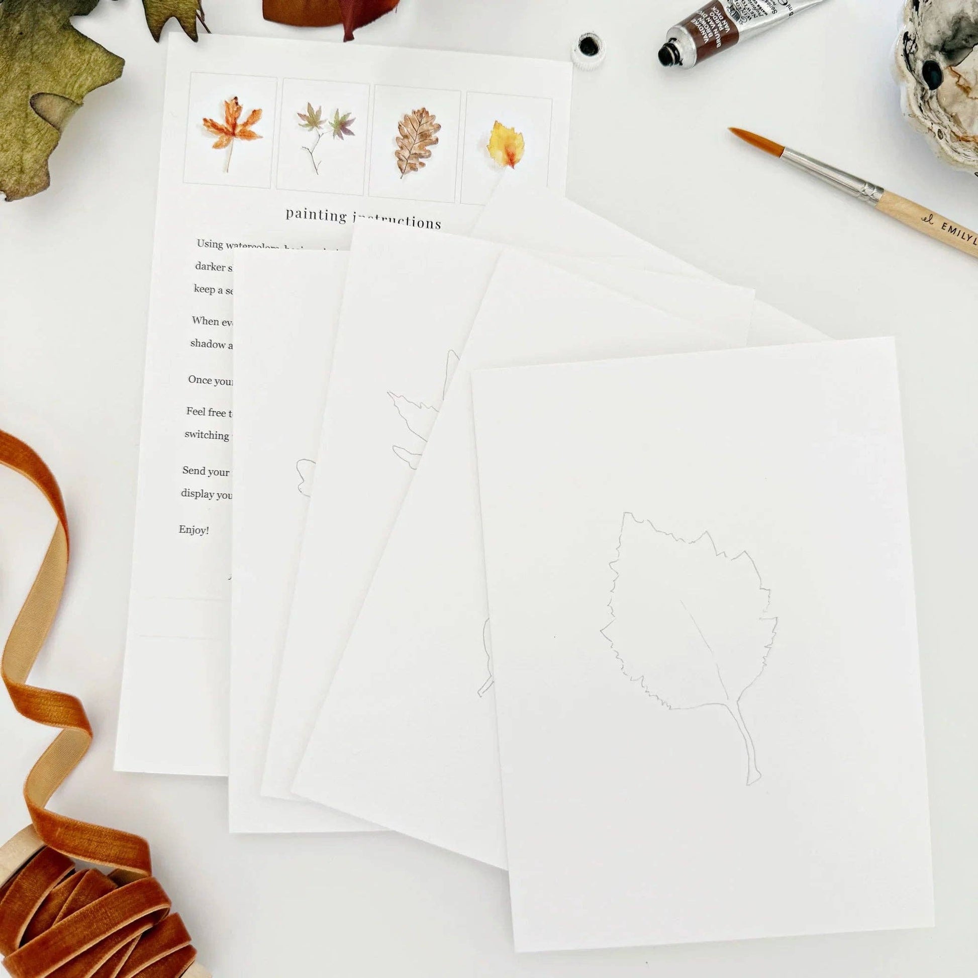 Fall Leaves Paintable Watercolor Notecard Set displayed with watercolor paints, brushes, and cozy autumn décor on a wooden table.