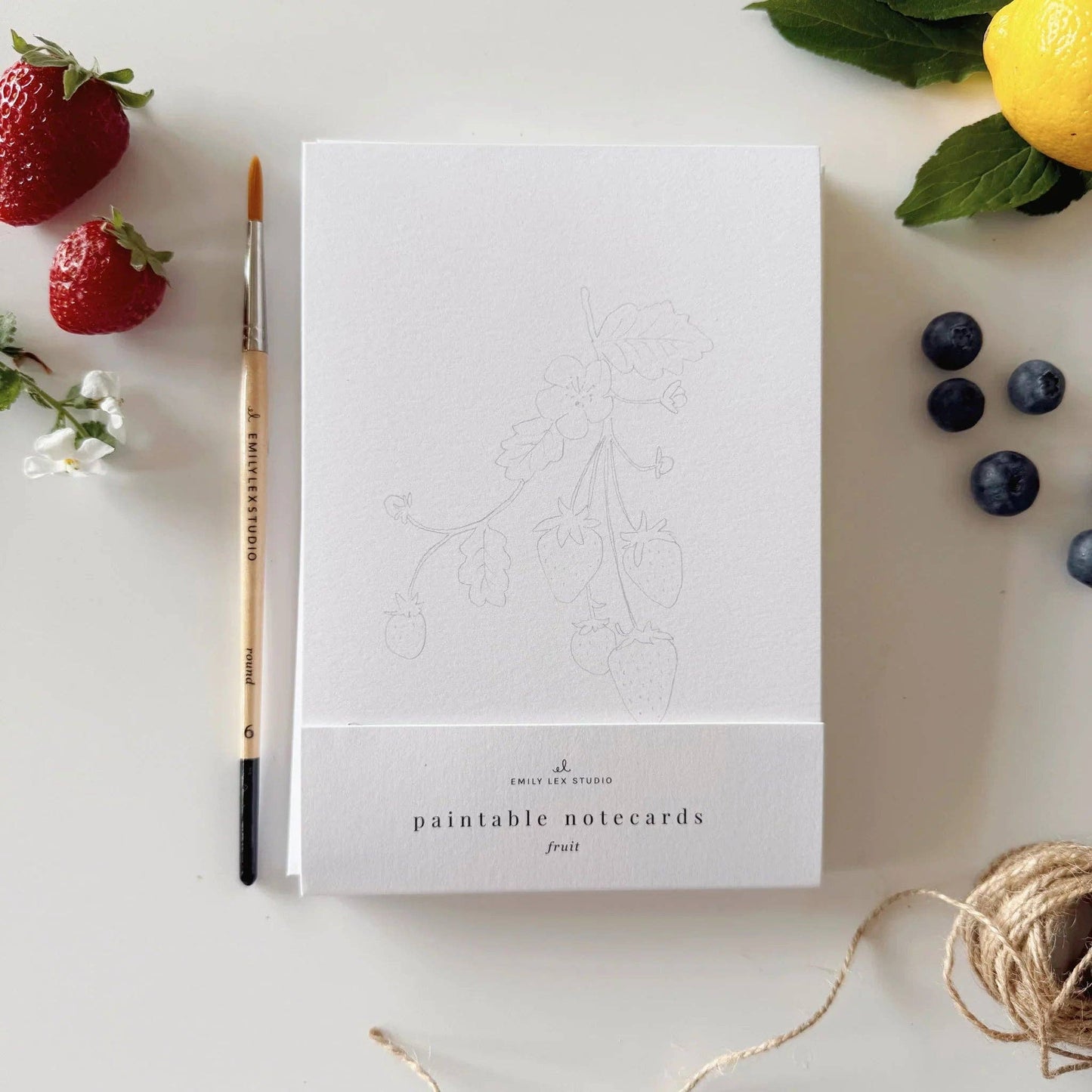 Paintable watercolor notecard set displayed with watercolor paints, brushes, and envelopes on a bright creative workspace.